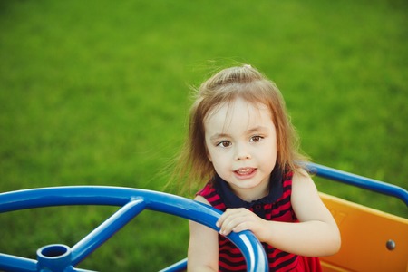 little girl spinning on a childrens carousel among the playground.の写真素材