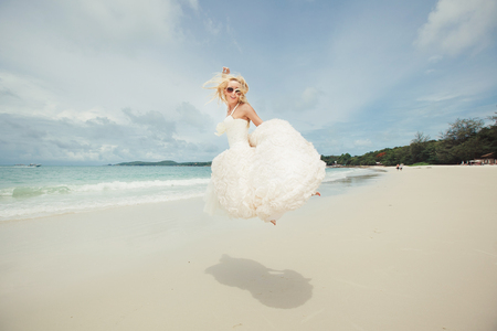 happy bride jumping in wedding dress at the sea. young happy woman on beach.の写真素材