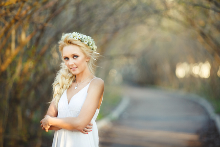 beautiful blond woman in white dress and floral wreath on her head. cute person in alley.の写真素材