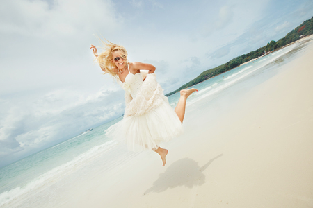 happy bride jumping in wedding dress at the sea. young happy woman on beach.の写真素材
