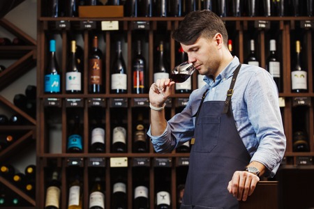 Bokal of red wine on background, male sommelier appreciating drink