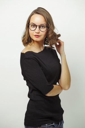 portrait of stylish woman in business look, wears black clothes and round spectacles, has a serious expression, stands on white isolated background.の写真素材