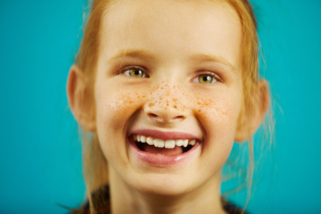 Laughing girl in good mood, has red hair and freckles, with nice facial features, on blue isolated...