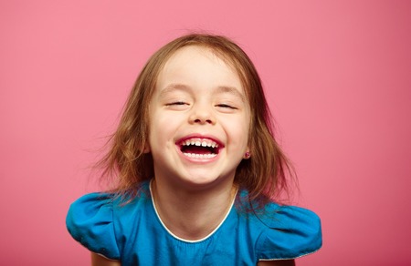 Frontal shot of laughter joyful little girl stands beside pink wall.の写真素材