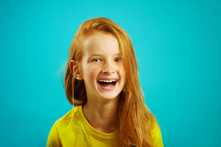 Sincere laughter of children girl with red hair on blue isolated. Happy child expresses a sincere emotion.の写真素材
