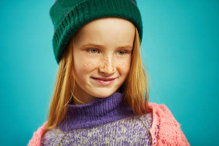 close up image of cute girl in winter sweater and hat on blue isolated background.