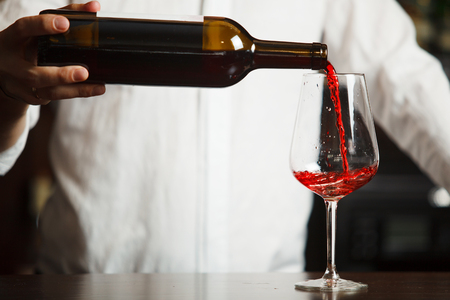 Male sommelier pouring red wine into long-stemmed wineglasses.の写真素材
