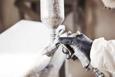 Close-up portrait of worker using spray gun and painting wood.