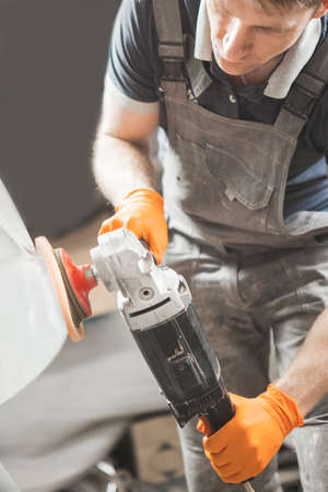 Worker with orbital polisher in auto repair shop. Car detailing. Final recovery of automobile.