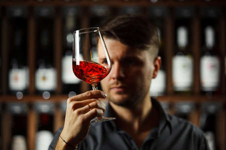 Bokal of red wine on background of male sommelier appreciating color, quality, flavor and sediments of drink. Professional degustation expert in winemaking.の写真素材