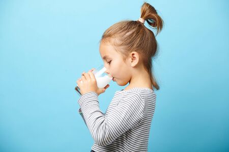 Child girl drinks milk without lactose, sideways portrait against blue isolated.の写真素材