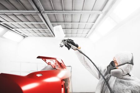Car painter sprays varnish in paint booth.