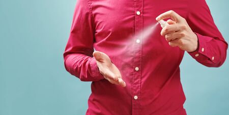 Close up image of man applying antiseptic spray to his hands for hygiene purposes. Portrait on blue...