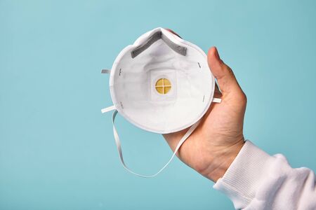 Human puts on respiratory antiviral medical mask,on blue isolated, point of view. Concept of safety and protection against respiratory viruses, coronavirus.の写真素材