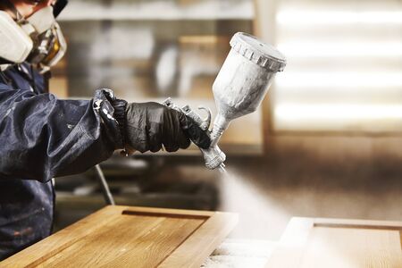 Close-up portrait of worker using spray gun and painting wood.の写真素材