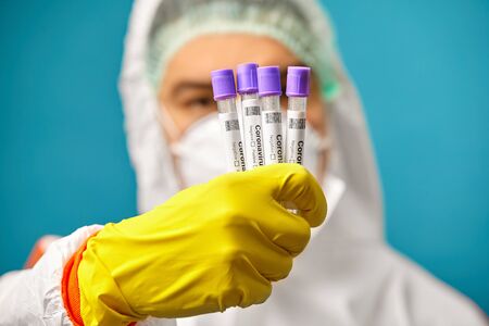 Close-up view of medical worker in protective coverall and respiatory mask holds a medical test...