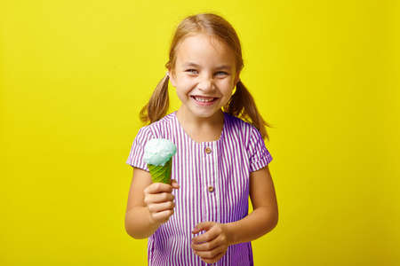 Image of five years old laughing little girl with ice cream, portrait on isolated yellow background.の写真素材