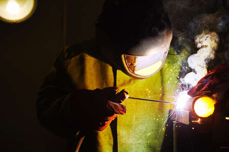 Worker in safety mask welds metal. Worker welding steel in industry with safety mask safety gloves...