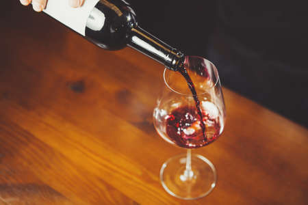 Closeup shot of glass with wine pouring by sommelierの写真素材
