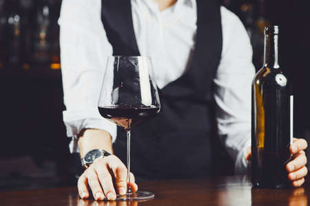 Bartender at the bar with a glass of red wine and bottle, close-up.の写真素材