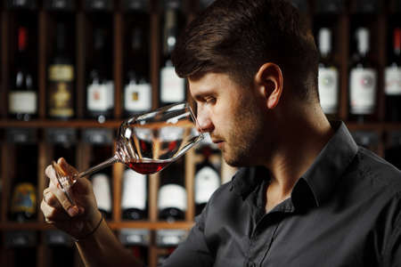 Bokal of red wine on background, male sommelier appreciating drink