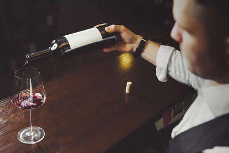 Male sommelier pouring red wine into long-stemmed wineglasses.の写真素材