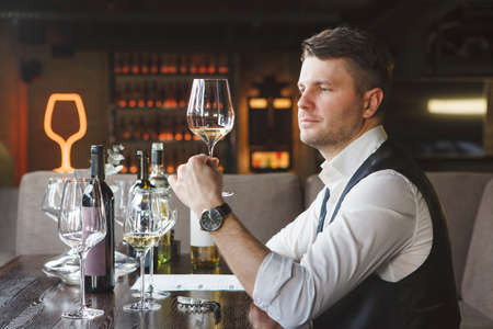 Sommelier looks at white wineglass at table in restaurantの写真素材