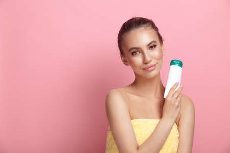 Female model holds plastic tube of lotion on pink backgroundの写真素材