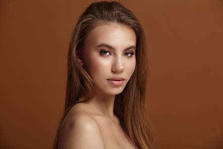 beauty glamor lifestyle. Seductive young woman with loose hair and bare shoulders posing for camera on brown background in studio close side viewの写真素材