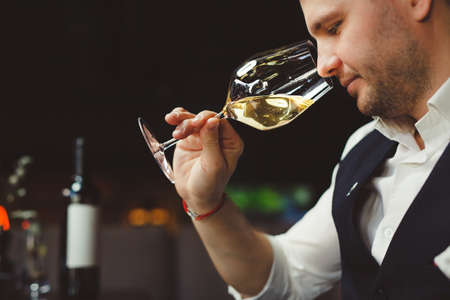 Sommelier smells white wine poured into glass at tableの写真素材