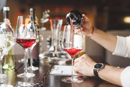 Faceless sommelier pours red wine into stem glass.の写真素材