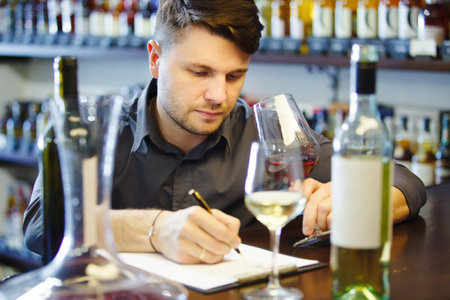 Male sommelier tasting red and white wine, making notes at bar counterの写真素材