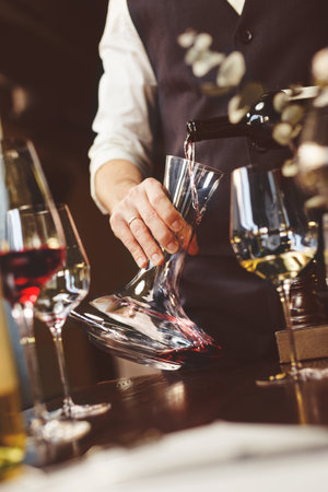 Faceless sommelier pouring wine into glass from decanter. Male waiter.の写真素材