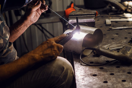 Industrial welder worker welding using argon machine, close up. Male in face mask welds with argon...