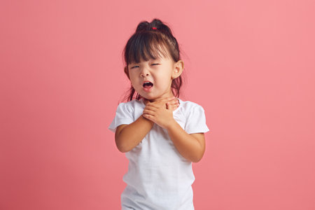 Frustrated little girl keeping throat and coughs having painful feelings or asthma attack.の写真素材