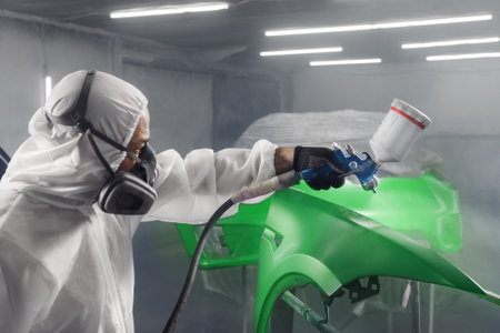 Car paint worker spraying green paint to car body element using spray gun in vehicle workshop chamber. Complex restoration of automobile body.の写真素材