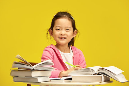 Photo of cheerful little Asian ethnicity first grader schoolgirl enjoying her reading time with...