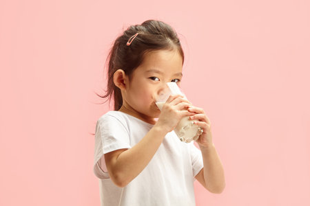 Pretty Asian Child Girl in White T Shirt Drinking Milk from Glass on Pink Isolatedの写真素材