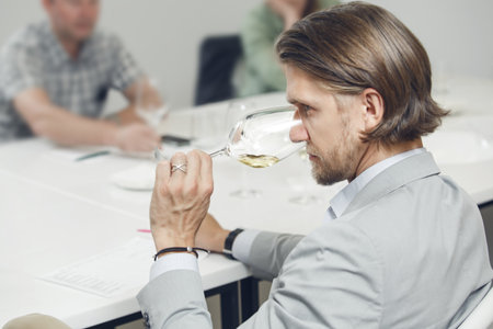 Wine experts association, sommelier school, professional development. Sommelier wearing in casual jacket tasting white wine from glass, analysing its taste, color, smell and acidity level.の写真素材