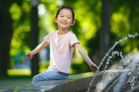 Happy Child Asian Girl Playing by Fountain in Green Park on Sunny Summer Dayの写真素材