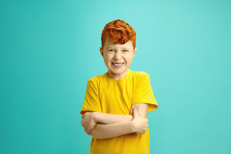 Capricious Red Haired Boy with Bared Teeth Looking to Camera, Clasping Hands in Front of him, Expressing Disagreement and Refusal to Cooperate and Dialogue, Having Protest Expression on Blue Isolatedの写真素材