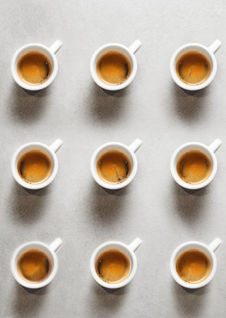 Nine Cups of Steaming Coffee Evenly Arranged in Neat Grid on Table Top Surface