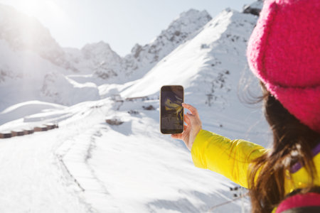 Woman Captures Snowy Mountain Scene on Her Phone at High-Elevation Peakの写真素材