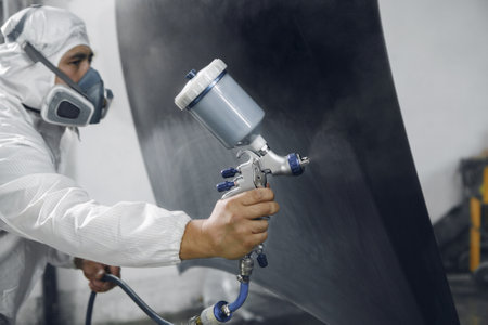Spray painter worker in protective glove with airbrush pulverizer varnishing and painting car body in paint chamber.の写真素材