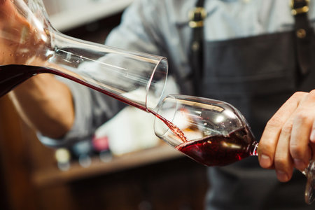 Sommelier pouring wine into glass from mixing bowl. Male waiter