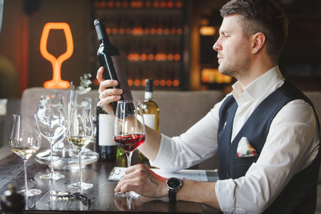 Wine steward holds wineglass, bottle of red beverage.の写真素材