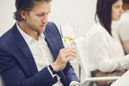 Adult male sommelier smelling and tasting white wine into glass during sommelier training.