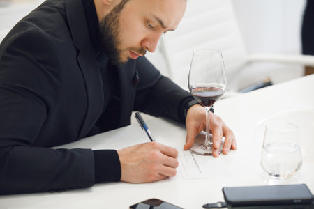 Focused Sommelier in Black Attire Analyzing Wine Color ad Taking Notes at Professional Tasting Courseの写真素材