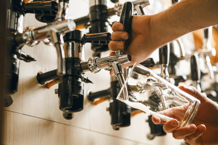 Pouring Cold Beer From Tap Into Clear Glass at Bar During Lively Evening Gathering Close upの写真素材