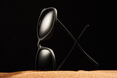 Rimmed sun glasses is on sand on black background.